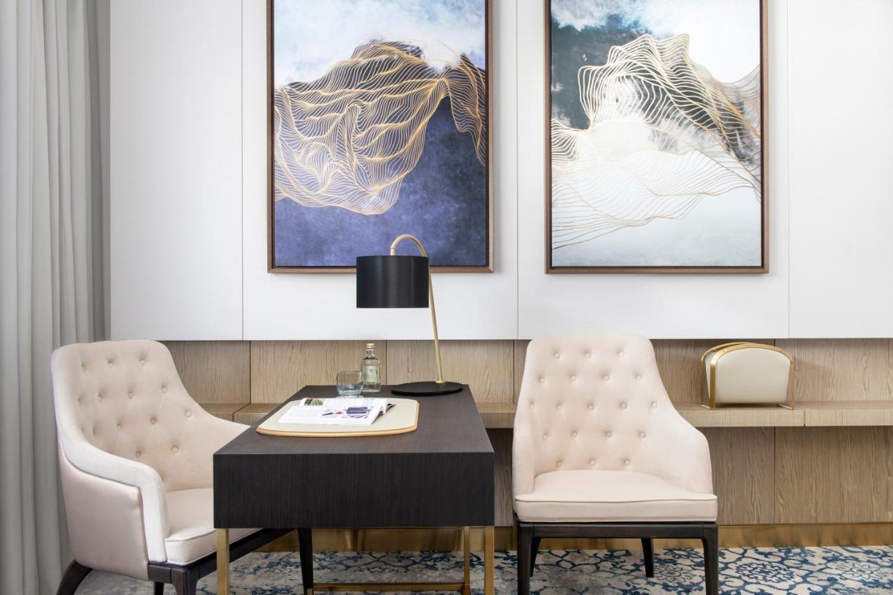 Steigenberger Hotel Доха Екстер'єр фото The photo shows a stylish and modern office space. There are two elegant framed artworks on the walls, characterized by abstract designs with soft colors and fluid lines. In the center, there’s a black desk with a white notepad and a pen. A sleek, bl