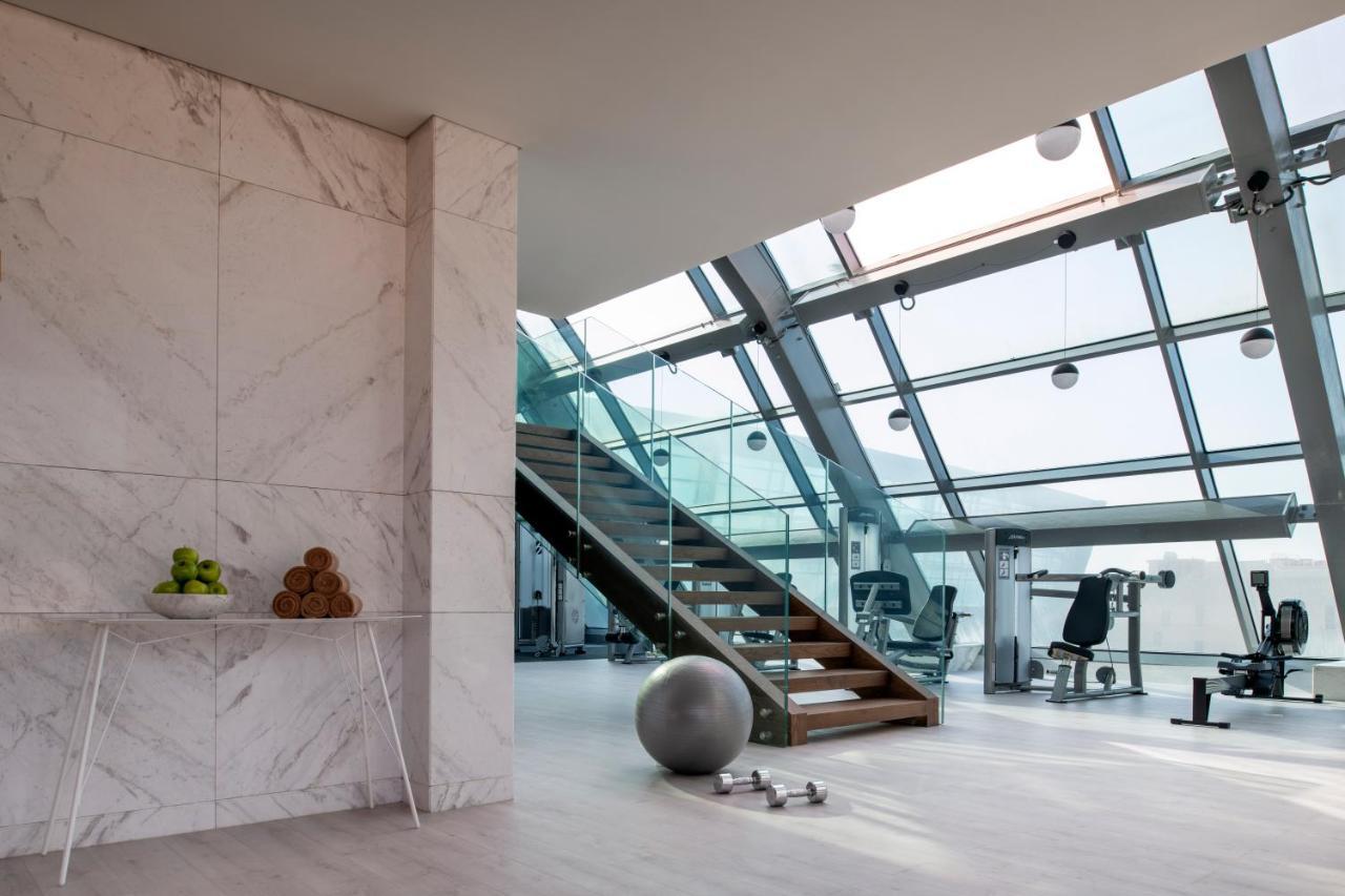 Steigenberger Hotel Доха Екстер'єр фото The photo showcases a modern, stylish interior space, likely a gym or fitness area. Key features include:

- **Large Windows**: The room is filled with natural light due to its expansive glass walls and ceiling.
- **Staircase**: A wooden staircase le