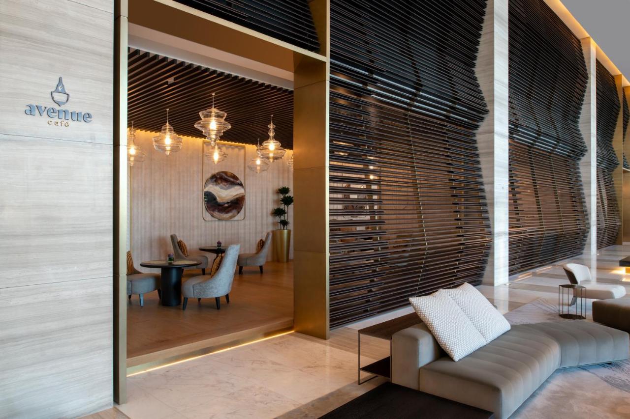 Steigenberger Hotel Доха Екстер'єр фото The photo shows a modern and elegant interior space of a café or restaurant. There is a large entrance framed in gold that leads into the café area, which features stylish furniture. Inside, you can see several chairs and tables, along with decorativ
