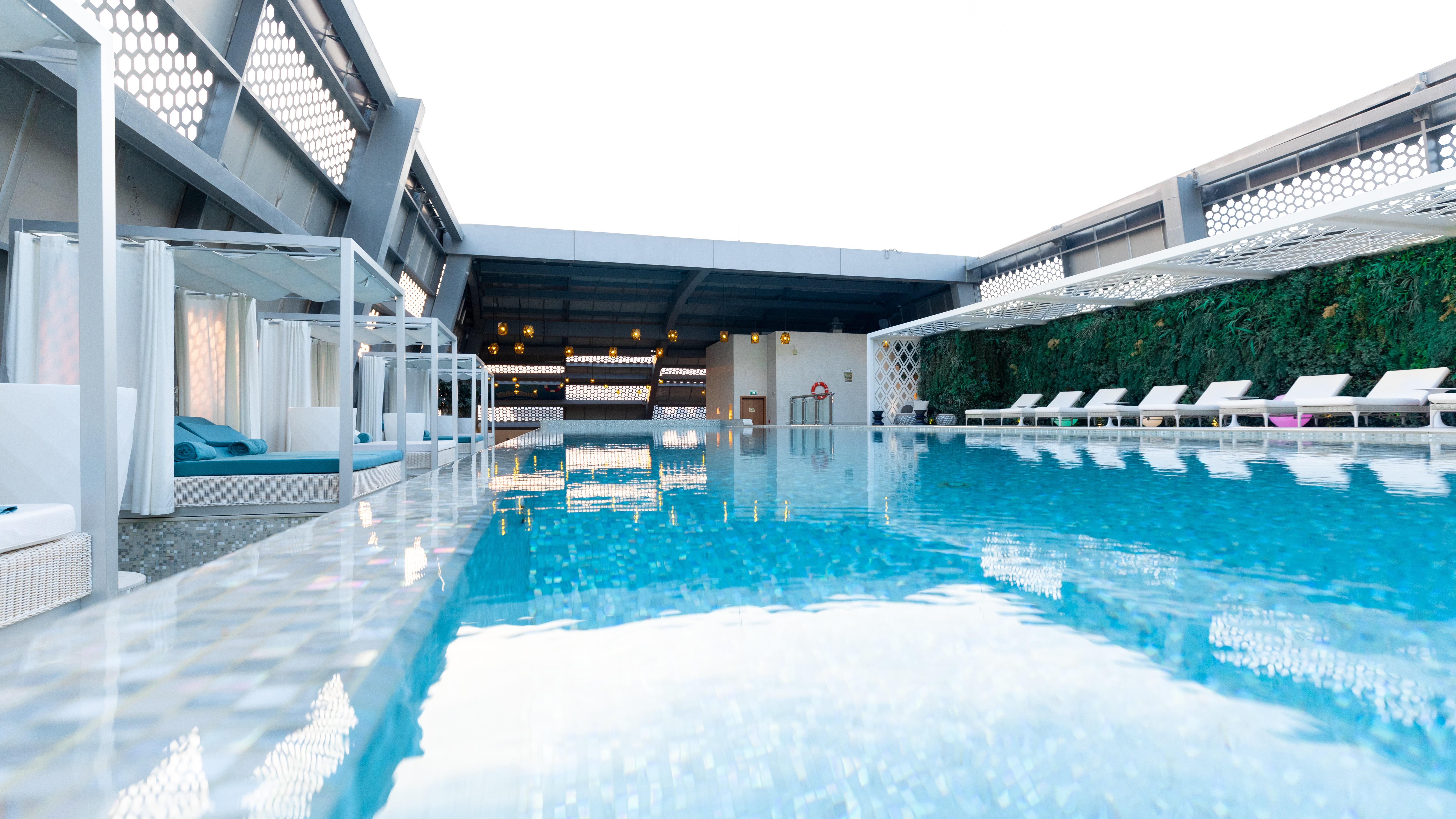 Steigenberger Hotel Доха Екстер'єр фото The photo shows a modern rooftop swimming pool. The water is clear and reflective, surrounded by white lounge chairs. There are canopies or cabanas along one side, providing shaded seating. The area has a sleek, contemporary design with a mixture of 