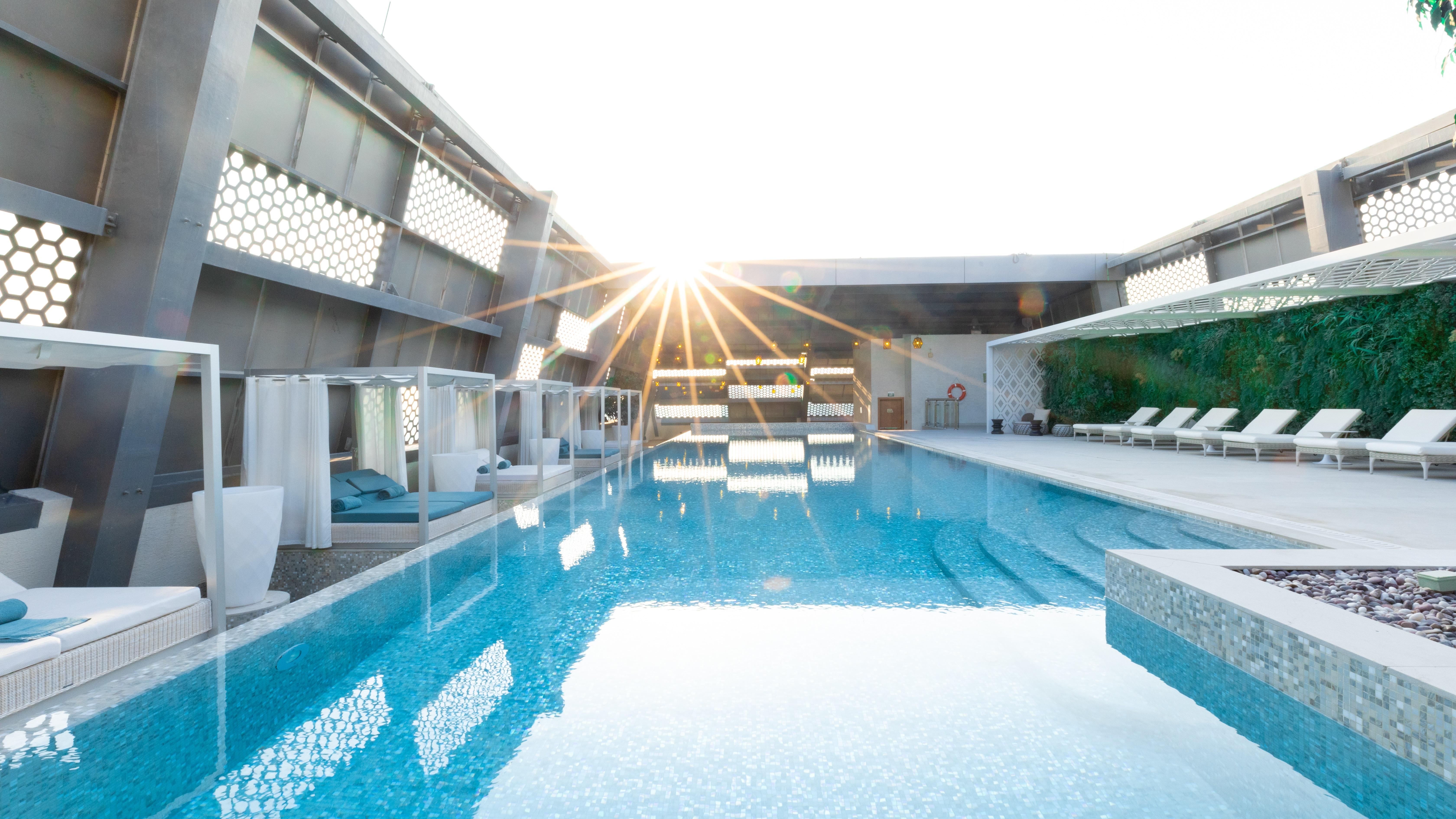 Steigenberger Hotel Доха Екстер'єр фото The photo shows a modern swimming pool area, likely located on a rooftop, with sunlight shining brightly in the background. The pool features clear, tranquil water that reflects the light and surrounding elements. There are comfortable lounge chairs 