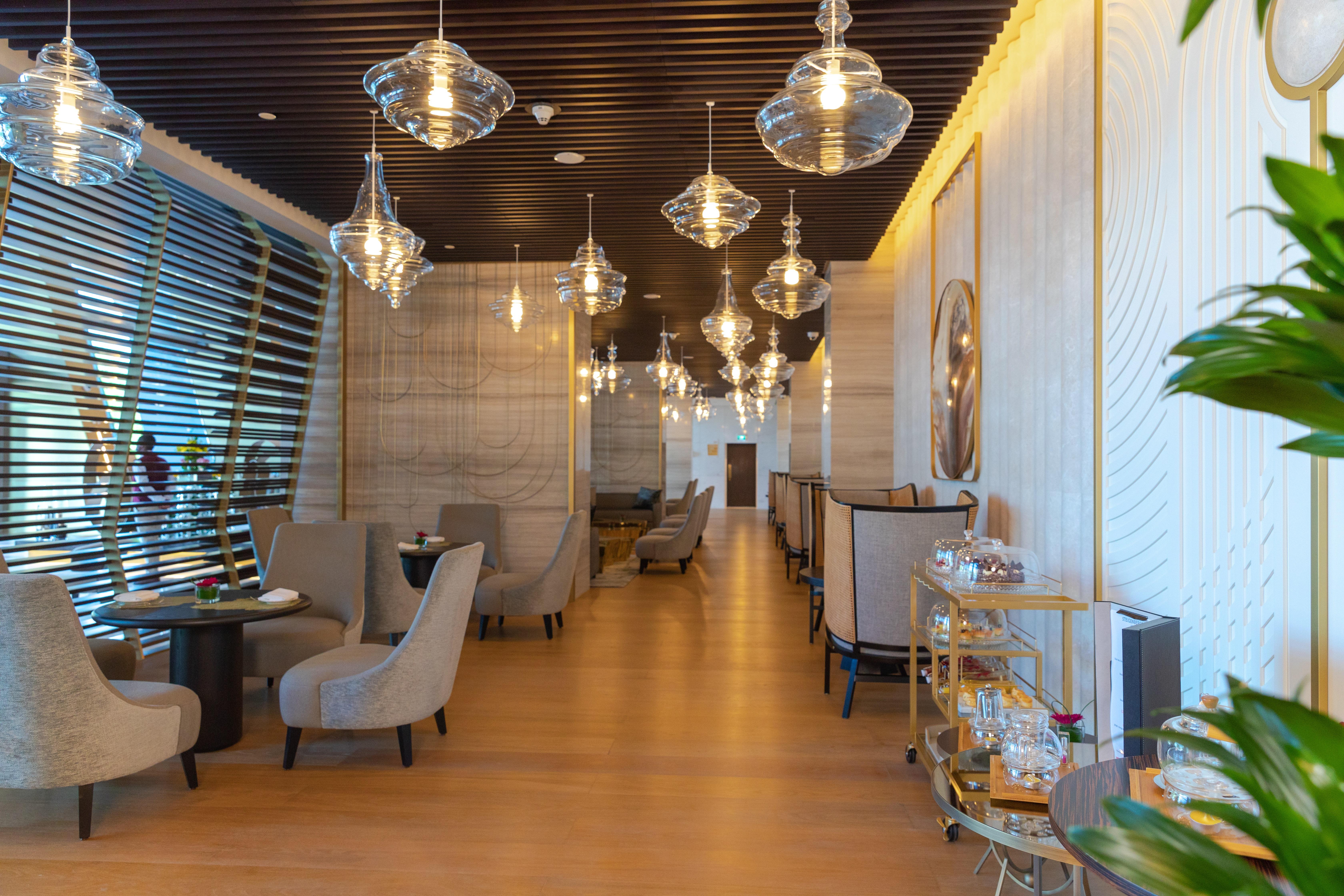 Steigenberger Hotel Доха Екстер'єр фото The photo shows the interior of a stylish restaurant. It features modern decor with elegant lighting, including several hanging glass pendant lamps. The seating area consists of plush armchairs arranged around small tables, creating an intimate atmos