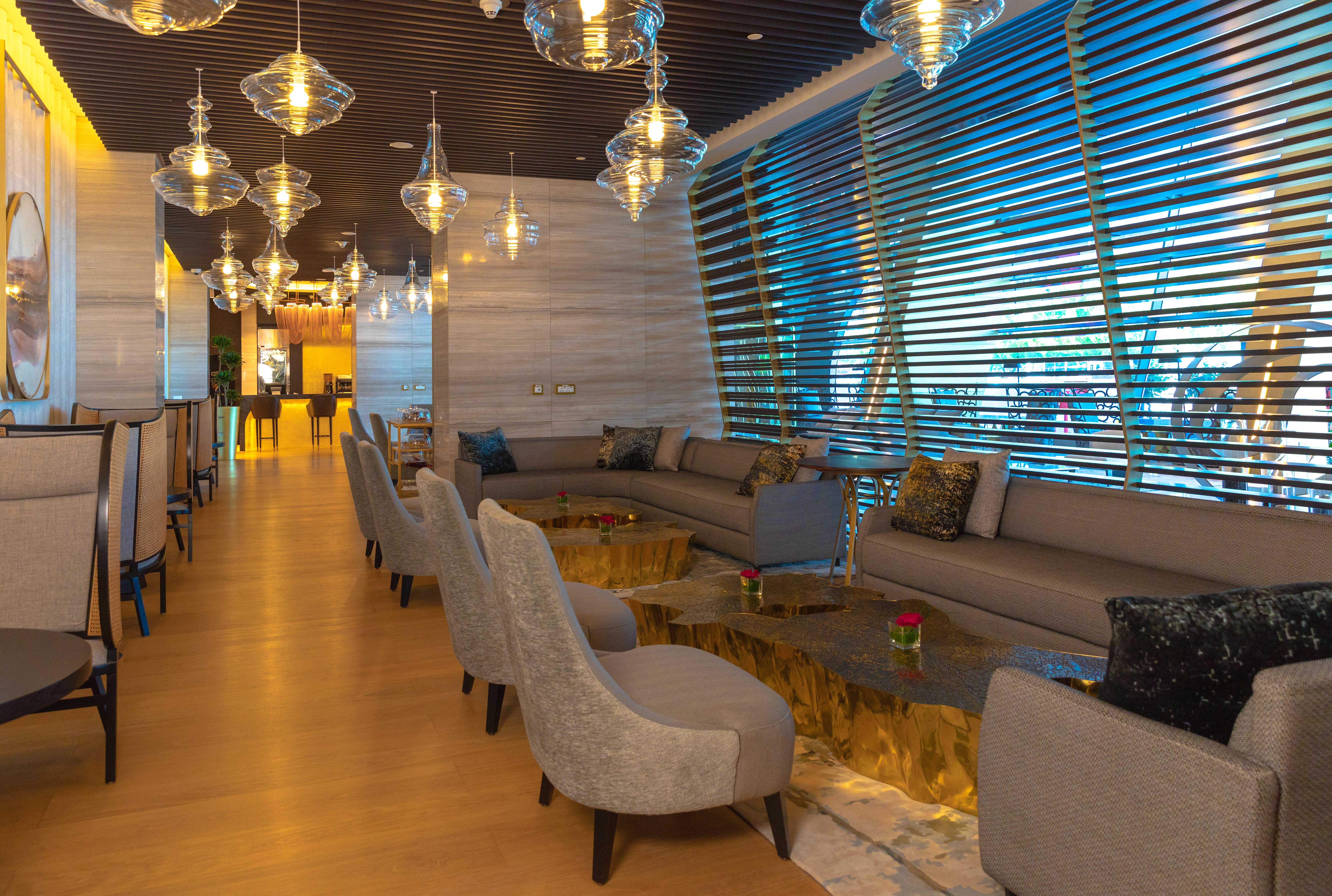 Steigenberger Hotel Доха Екстер'єр фото The photo depicts a modern and stylish lounge area. It features a spacious layout with comfortable seating arrangements, including beige sofas and stylish chairs. The tables have a unique design, with a gold-colored base. Ambient lighting is provided