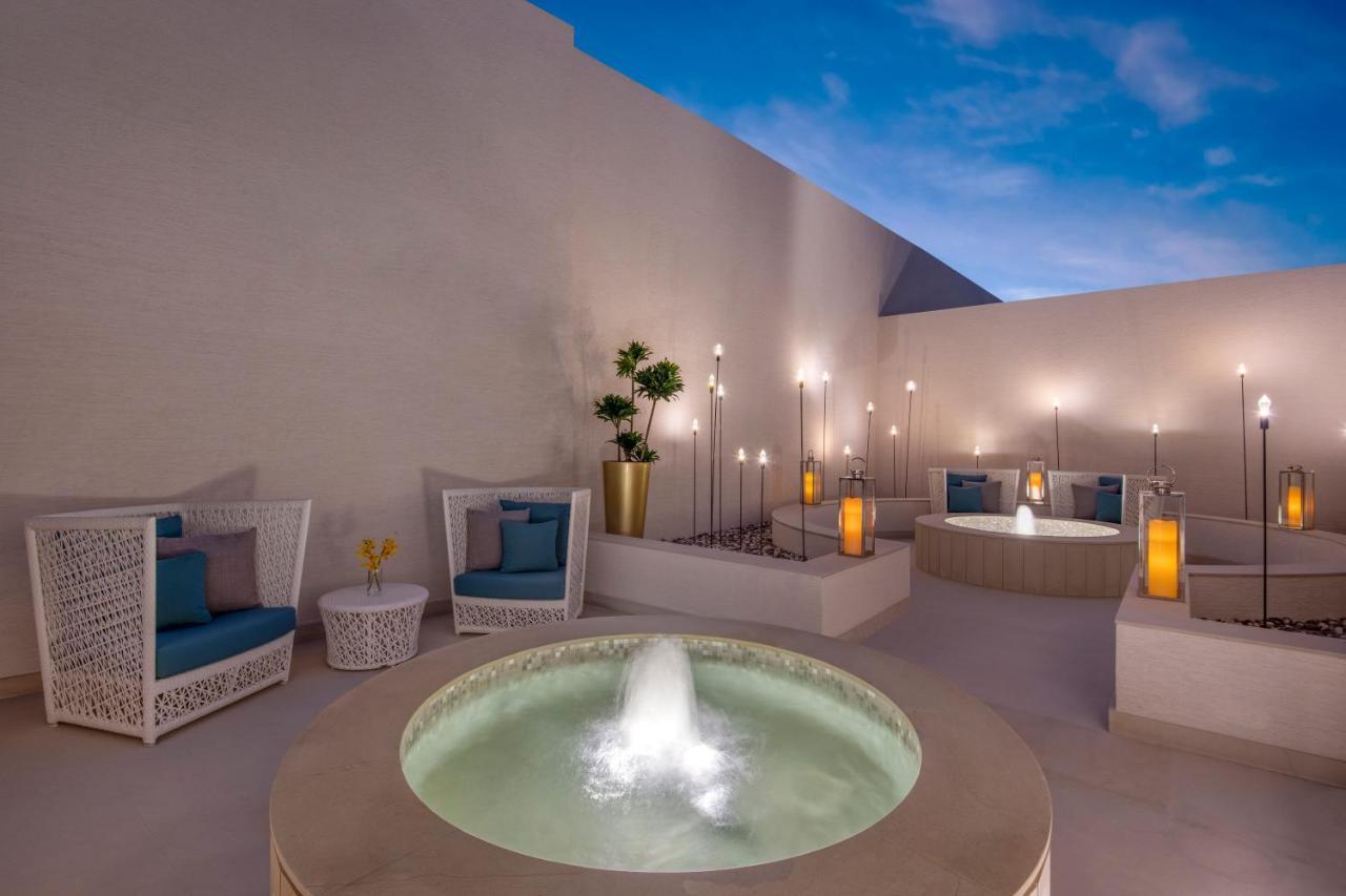 Steigenberger Hotel Доха Екстер'єр фото The photo depicts a serene outdoor space featuring a modern and stylish design. Central to the image is a round stone fountain with water gently flowing from it, creating a tranquil atmosphere. Surrounding the fountain are comfortable seating areas w