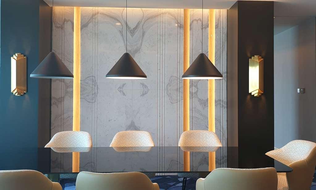 Steigenberger Hotel Доха Номер фото The photo showcases a modern interior space featuring a sleek design. The focal point is a wall adorned with a marble-like texture, enhanced by vertical lighting strips that add warmth to the environment. Above a table or counter are three pendant li