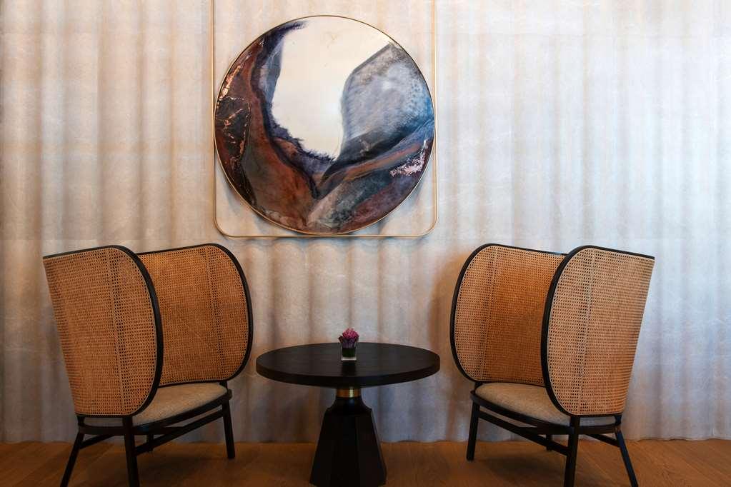 Steigenberger Hotel Доха Ресторан фото The photo showcases a stylish and modern seating area featuring two elegantly designed chairs with curved, woven backs and light-colored cushions. Between the chairs is a small round table with a black base. Above the table hangs a large circular art